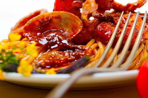 Italian seafood spaghetti pasta on red tomato sauce over white rustic wood table