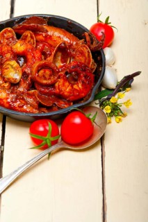 Fresh seafood stew prepared on an iron skillet ove white rustic wood table