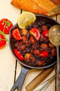 Baby cuttle fish roasted on iron skillet with tomatoes and onions over rustic wood table