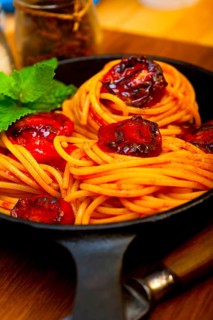 Italian spaghetti pasta and tomato with mint leaves on iron skillet over wood board