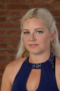 Pretty young woman with freckles and long blond hair in a sleeveless dress in front of a red brick wall