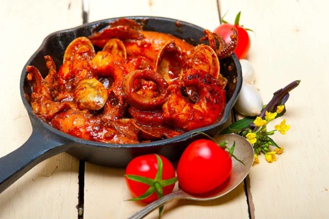 Fresh seafood stew prepared on an iron skillet ove white rustic wood table