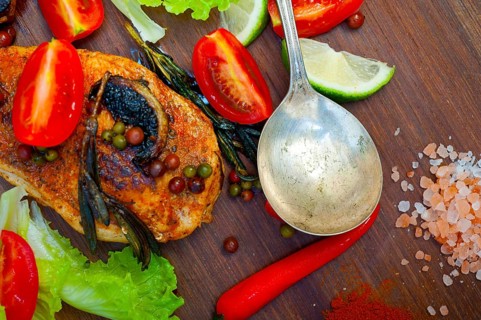 Wood fired hoven cooked chicken breast on wood board with herbs spices and vegetables