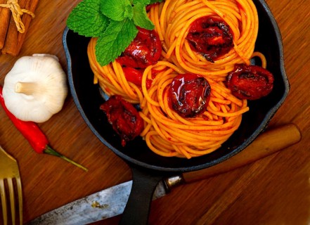 Italian spaghetti pasta and tomato with mint leaves on iron skillet over wood board