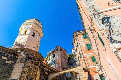 The steeple of the church of Santa Margherita di Antiochia and nested houses built into the hillside with pastel-coloured facades