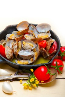 Fresh clams stewed on an iron skillet over wite rustic wood table