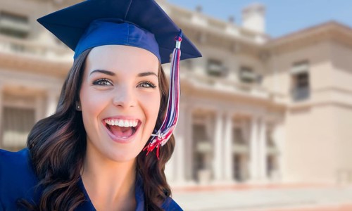 Happy graduating mixed-race woman in cap and gown celebrating on campus