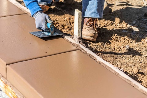 Construction worker using stainless steel edger on wet cement forming coping around new pool