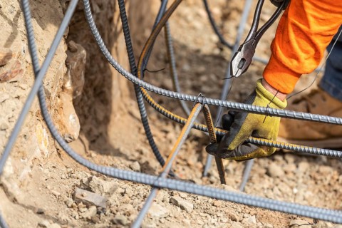 Worker securing steel rebar framing with wire plier cutter tool at construction site