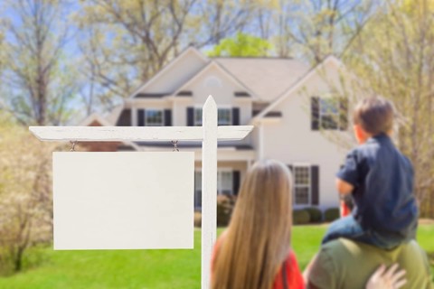 mixed-race young family in front of blank real estate sign and new house