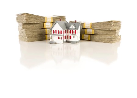 Stacks of one hundred dollar bills with small house on slight reflective surface