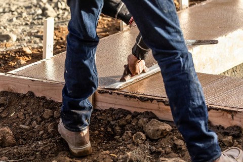 Construction worker using wood trowel on wet cement forming coping around new pool