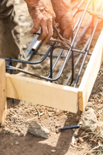 Worker securing steel rebar framing with wire plier cutter tool at construction site