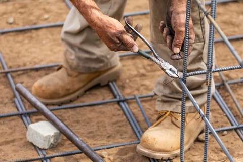 Worker securing steel rebar framing with wire plier cutter tool at construction site