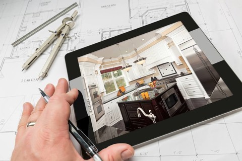 Hand of architect on computer tablet showing custom kitchen photo over house plans