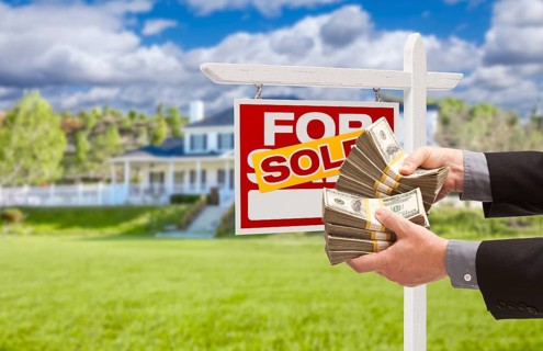 Man handing over thousands of dollars in front of house and sold for sale real estate sign