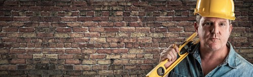 Male contractor in hard hat holding level in front of old brick wall banner with copy space