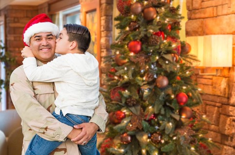 Hispanic armed forces soldier wearing santa hat hugging son in front christmas tree