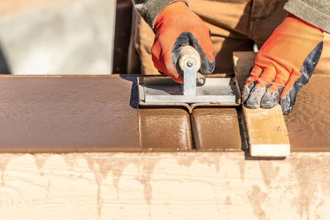 Construction worker using hand groover on wet cement forming coping around new pool