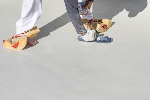Worker wearing sponges on shoes smoothing wet pool plaster with trowel