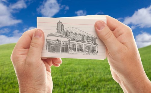 Male hands holding stack of paper with house drawing over empty grass field and sky