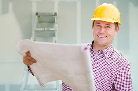 Smiling contractor holding blueprints inside home construction site
