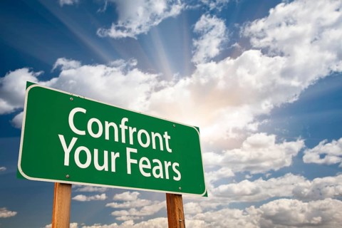Confront your fears green road sign with dramatic clouds and sky