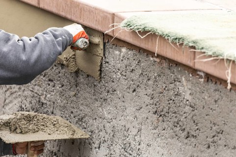 Tile worker applying cement with trowel at pool construction site