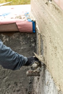 Tile worker applying cement with trowel at pool construction site
