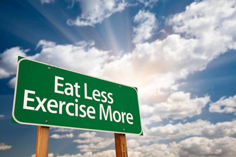Eat less exercise more green road sign with dramatic clouds