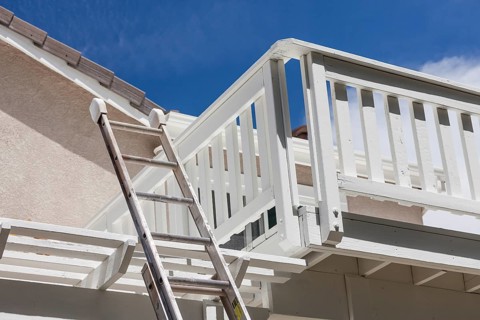 Construction ladder leaning on white house deck with blue sky behind