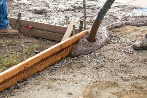Construction worker pooring wet deck cement into wooden frame