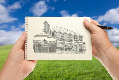 Male hands holding pen and pad of paper with house drawing over empty grass field and sky