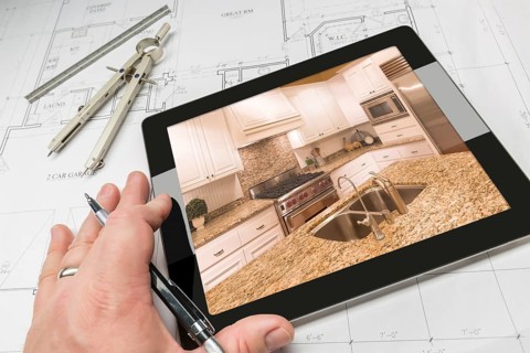 Hand of architect on computer tablet showing custom kitchen photo over house plans