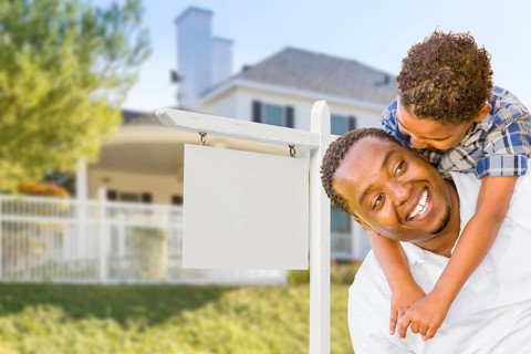 Happy african american father and mixed-race son in front of blank real estate sign and new house