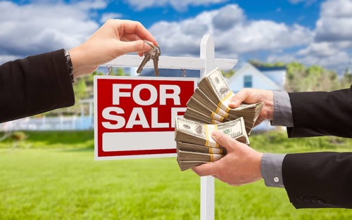 Man handing woman thousands of dollars for keys in front of house and for sale real estate sign