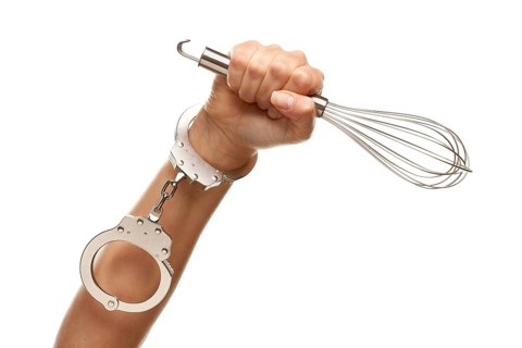 Handcuffed woman holding egg beater in the air isolated on a white background