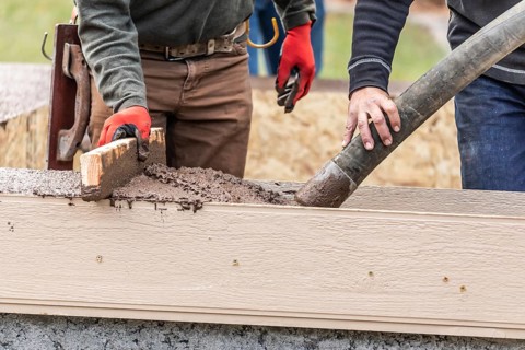 Construction workers pouring and leveling wet cement into wood framing