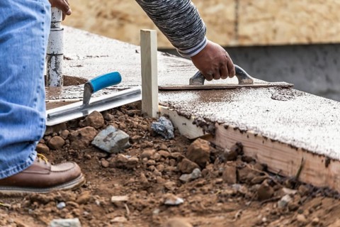 Construction worker using wood trowel on wet cement forming coping around new pool