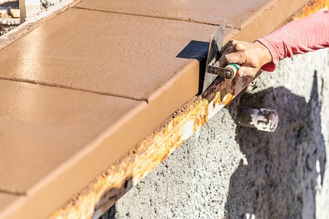Construction worker using stainless steel edger on wet cement forming coping around new pool