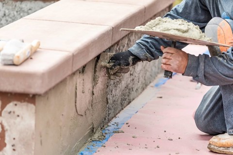 Tile worker applying cement with trowel at pool construction site