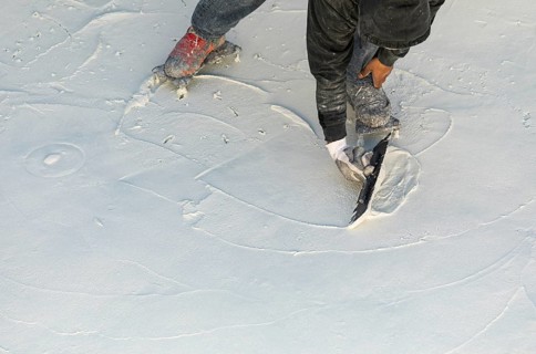 Worker wearing spiked shoes smoothing wet pool plaster with trowel