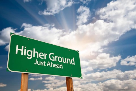 Higher ground green road sign against dramatic sky