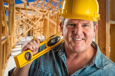 Smiling contractor in hard hat holding level and pencil at construction site