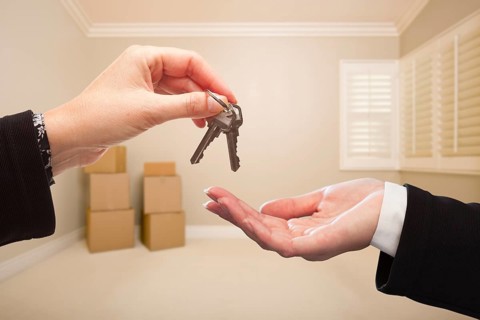 Woman handing over the house keys to A new home inside empty tan colored room
