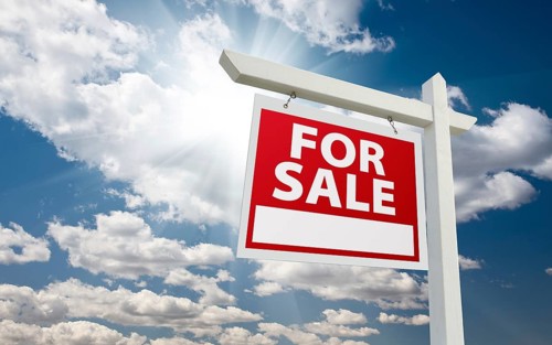 For sale real estate sign over clouds and blue sky with sun rays