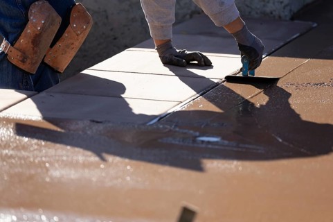Construction worker smoothing wet cement with hand edger tool