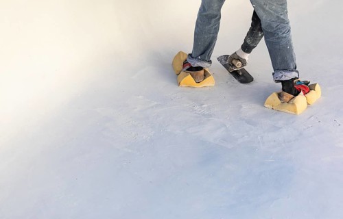Worker wearing sponges on shoes smoothing wet pool plaster with trowel