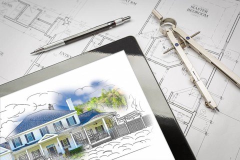 Computer tablet showing house illustration sitting on house plans with pencil and compass