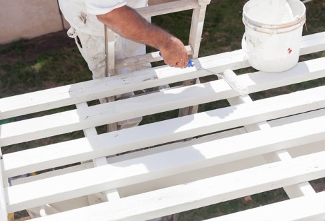 Painter rolling white paint onto the top of A home patio cover